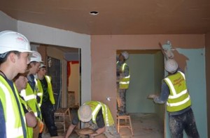 Students watch as a wall is being plastered