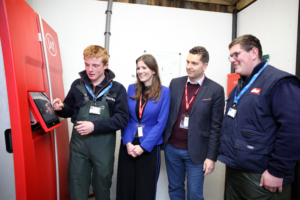 Stockperson apprentice George Matthews demonstrates the robotic milking system to Minister of State for Higher & Further Education Michelle Donelan, MP Edward Timpson CBE and fellow apprentice Oliver Riley