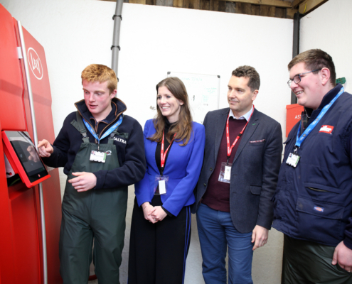 Stockperson apprentice George Matthews demonstrates the robotic milking system to Minister of State for Higher & Further Education Michelle Donelan, MP Edward Timpson CBE and fellow apprentice Oliver Riley