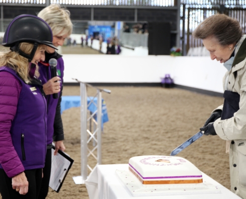 The Princess Royal cuts a cake, watched by Sheila Saner and Eleanor Dixon