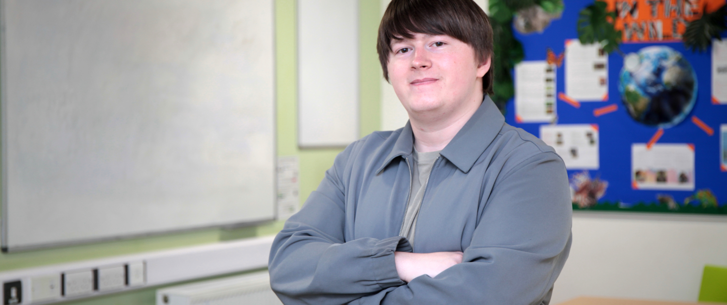 Declan Beadle, a Reaseheath Supported Intern and Student Ambassador, smiling with arms crossed in a Foundation Studies classroom.