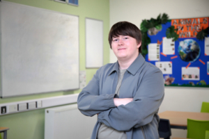 Declan Beadle, a Reaseheath Supported Intern and Student Ambassador, smiling with arms crossed in a Foundation Studies classroom.