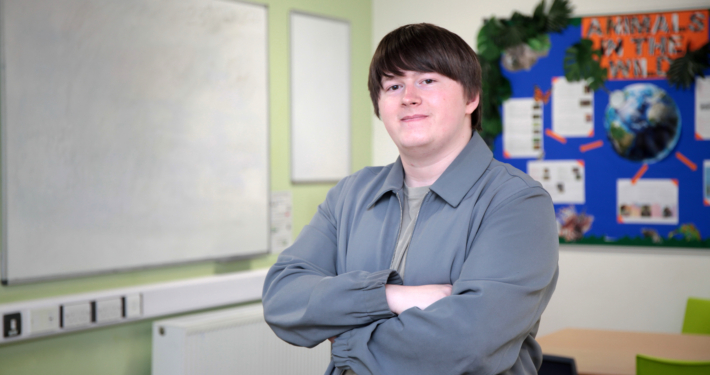 Declan Beadle, a Reaseheath Supported Intern and Student Ambassador, smiling with arms crossed in a Foundation Studies classroom.