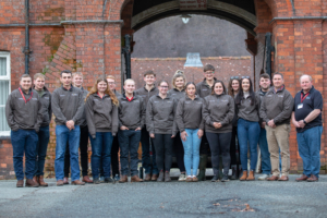The full cohort of sixteen delegates, including Reaseheath’s own farm team members Lucy Szolkowska and Drew Gerry, stand together outside the college. These young leaders represent the future of professional dairy farming.