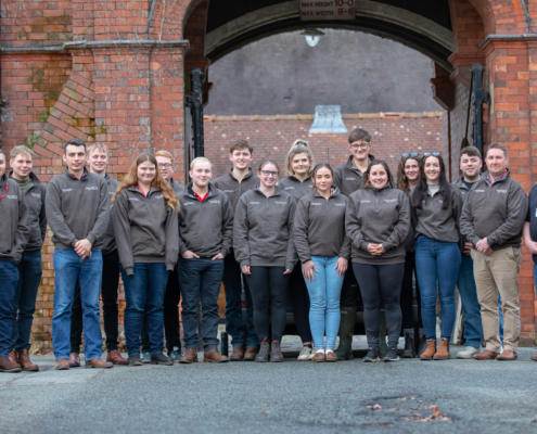 The full cohort of sixteen delegates, including Reaseheath’s own farm team members Lucy Szolkowska and Drew Gerry, stand together outside the college. These young leaders represent the future of professional dairy farming.